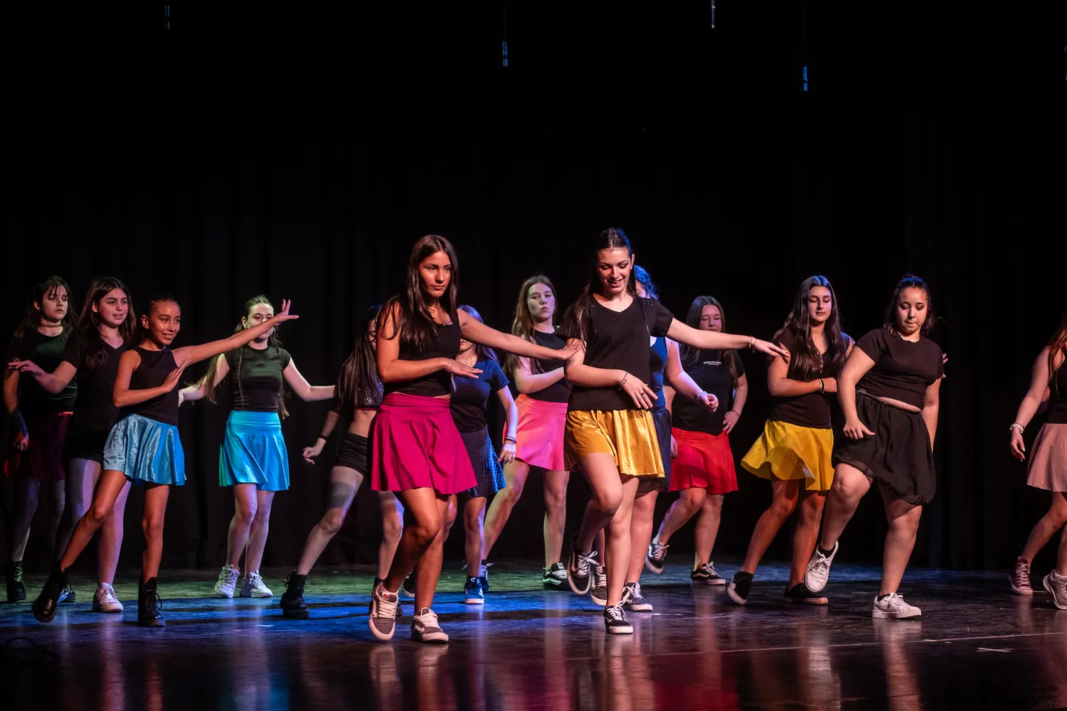 Alumnas del colegio bailando sobre el escenario en una muestra, con polleras de colores.